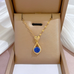 Détail du collier doré avec pierre bleue en forme de goutte et cœur dans un écrin