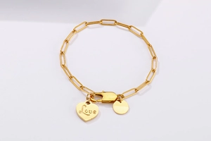 Detailed close-up of gold paperclip chain bracelet with heart Love and round charms