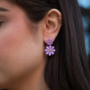 Close-up of purple daisy enamel earrings worn by a model in outdoor natural light