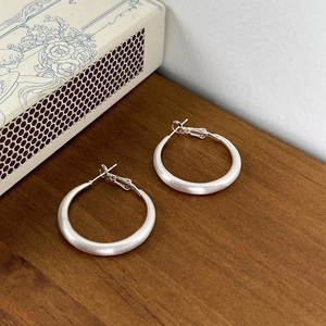 Close-up of silver-tone circular earrings with matte finish on a rustic wooden surface