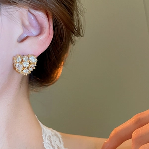 Close-up of elegant 18k gold heart stud earrings with zircon crystals on female model