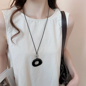 Detail of a minimalist black oval resin pendant on a long rope chain with a silver clasp