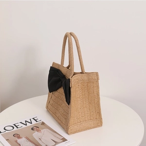 Beige straw tote bag with large black ribbon bow for elegant summer beach vacations