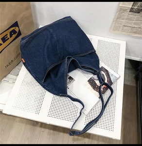Detail of dark blue denim tote bag with adjustable strap on a white display board