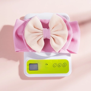 Detailed view of pink and beige bow headband on digital scale weighing 27.8g