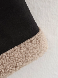 Detailed view of black suede fabric and thick creamy white faux shearling wool lining