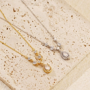 Detailed view of silver and gold teardrop pendant necklaces on a textured stone surface