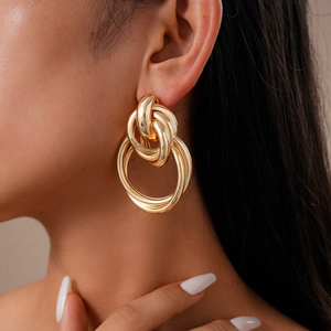Close-up of golden geometric knotted metal earrings worn by a model in natural light