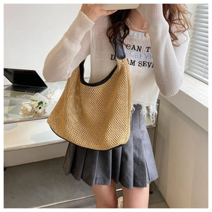 Close-up of khaki woven tote bag with black leather shoulder straps on a white sweater