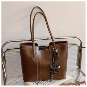 Close-up of brown tote bag with contrast stitching and decorative cartoon pendants