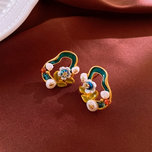 Detail of flower earrings with gold finish, colorful enamel, and pearls on velvet
