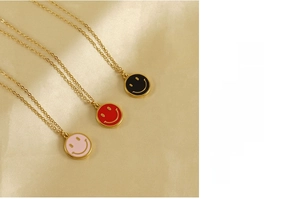 Trois colliers dorés avec pendentifs smiley en émail noir, rouge et rose sur soie
