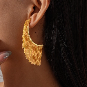Detail of elegant gold beaded tassel earrings on model showing metal chain texture
