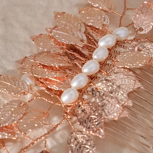 Rose gold bridal hair comb with metallic leaf design and white pearls on soft fabric