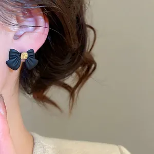 Elegant black bow stud earrings with gold center buckle shown on model side profile view