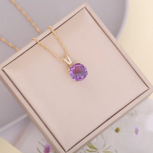 Close-up of a faceted purple crystal pendant on a gold chain over a beige jewelry box