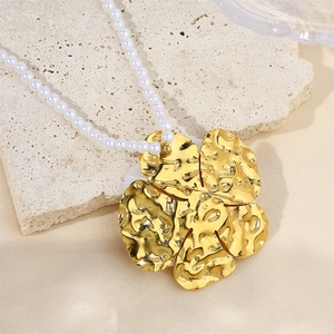 Macro shot of gold-plated flower pendant with white pearls on a textured background
