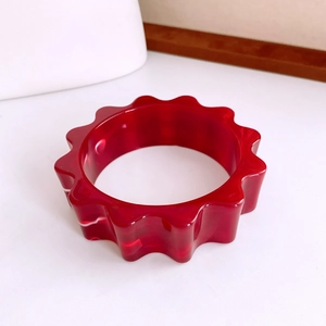 Gros plan d'un large bracelet en résine rouge avec bords ondulés et texture marbrée