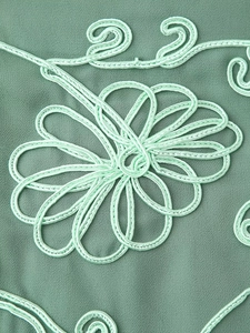 Détail macro d'une broderie florale vert clair et de motifs de cordes sur le tissu