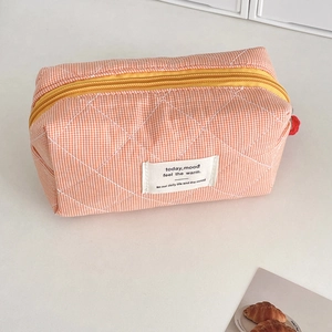 Detailed close-up of quilted orange plaid cosmetic bag with vibrant yellow zipper closure