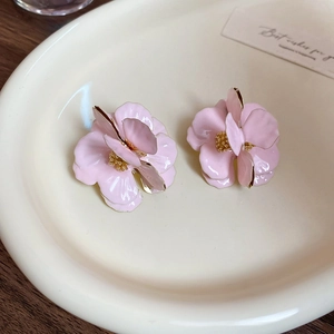 Pink layered flower earrings with gold edges on white ceramic dish and wood background