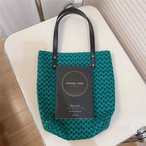 Detail view of green geometric print tote bag with black leather straps on white chair