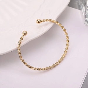 Minimalist gold twisted cable open cuff bracelet with spherical ends on white porcelain