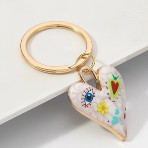 Détail du porte-clés coeur doré avec œil bleu et motifs floraux en émail sur socle blanc