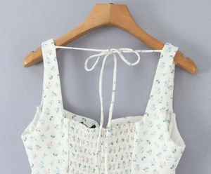 Détail de l'encolure carrée et des bretelles nouées sur une robe fleurie blanche à smocks
