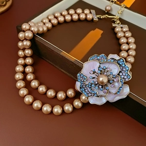 Detail of a double-layer pearl necklace featuring a pink enamel flower pendant with crystals