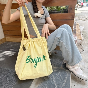 Close-up of yellow drawstring tote bag with green Bonjour lettering and wide strap