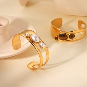 Detail of gold hollow open bangles featuring natural tiger eye stones and faux pearls