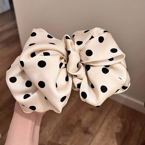 Close-up of a large cream-white polka dot bow hair clip with a silky texture finish