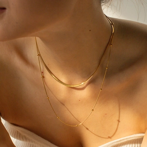 Close-up of double-layered gold necklace with flat snake chain and beaded detail on model