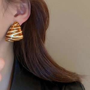 Macro shot of triangular gold-plated earrings with amber enamel patterns on model
