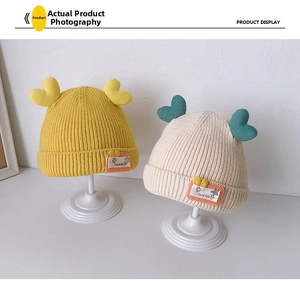 Detail of yellow and beige knitted baby hats with heart tops and Good Life labels