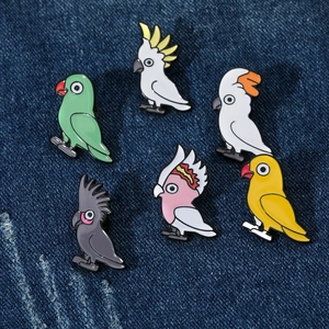Détail de six épingles en émail de perroquets colorés sur un tissu en denim bleu
