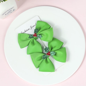Detail of Christmas green bow hair clips with red berries and holly leaves on card