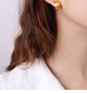 Detail of elegant matte gold C-shaped titanium hoop earrings worn by a model