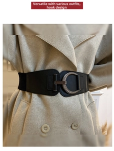 Close-up of black wide elastic waist belt with silver circular metal buckle on a beige coat