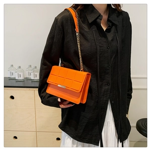 Close-up of orange quilted crossbody bag with gold chain strap worn by a model