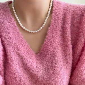 Close-up of elegant white pearl necklace worn with a pink mohair sweater texture
