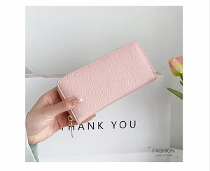 Pink pebbled faux leather long wallet with gold zipper detail held in hand
