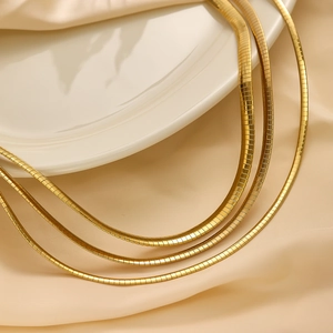 Close-up of flexible 18k gold plated flat snake chain necklaces on silk fabric