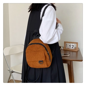 Side view of caramel corduroy mini backpack worn by model in a minimalist indoor setting