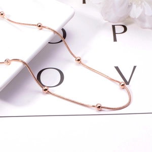 Detail of rose gold snake chain necklace featuring polished beads on white background
