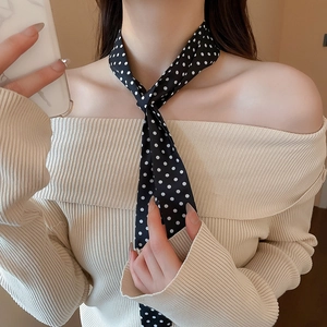 Close-up of a classic black silk scarf with white polka dots tied around the neck