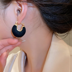 Close-up of black flocked U-shaped earrings with gold metal trim worn by model