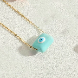 Macro view of a gold chain with a rectangular light blue evil eye pendant on a white background