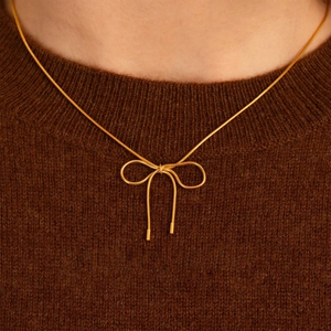 Minimalist gold bow pendant necklace on a thin snake chain worn by a female model